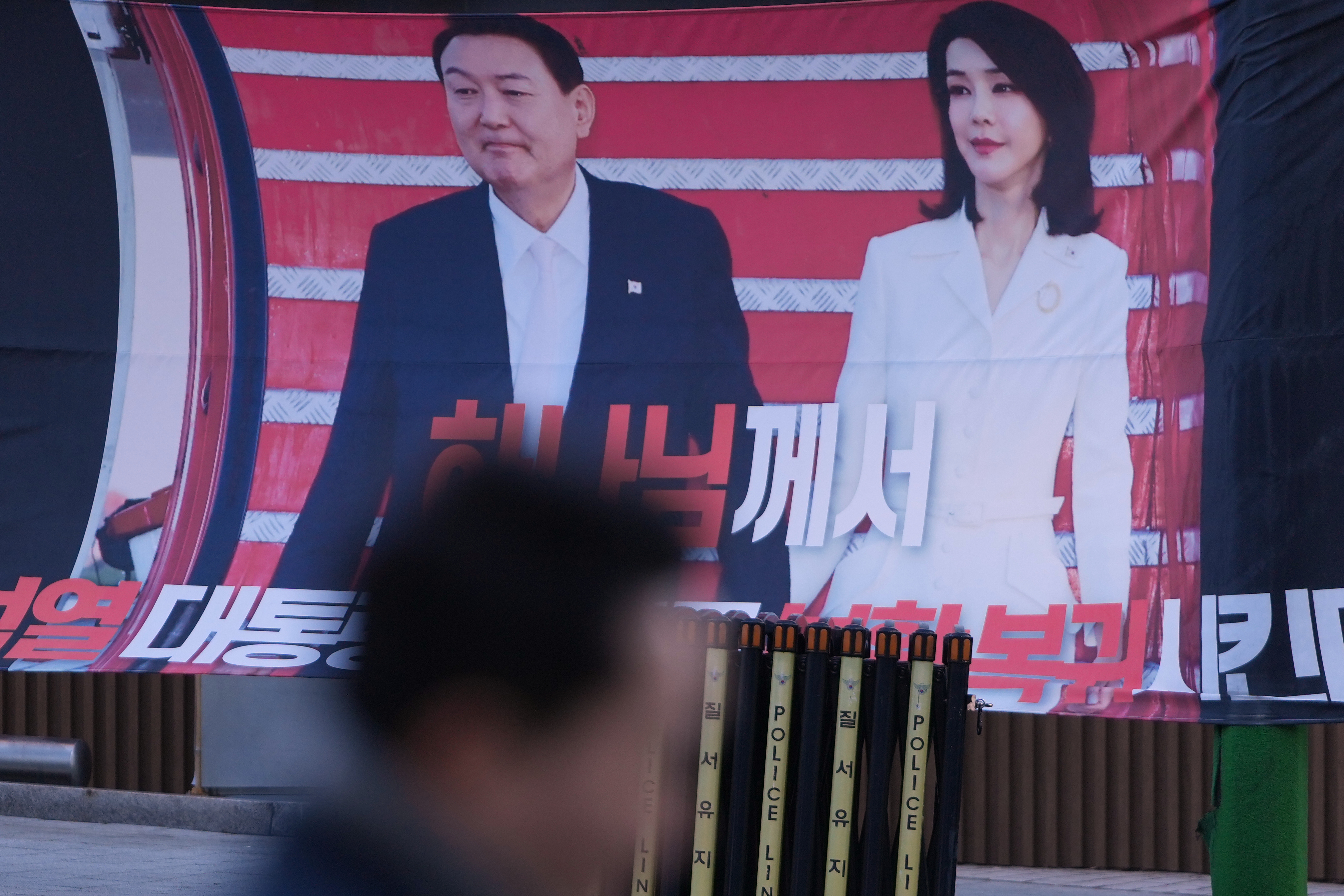 A man walks past near a banner showing the picture of former South Korean President Yoon Suk Yeol and his wife Kim Keon Hee, outside of Seoul Central District Court, in Seoul, South Korea, Jan. 13. The former first lady was sentenced to 20 months in prison for corruption.