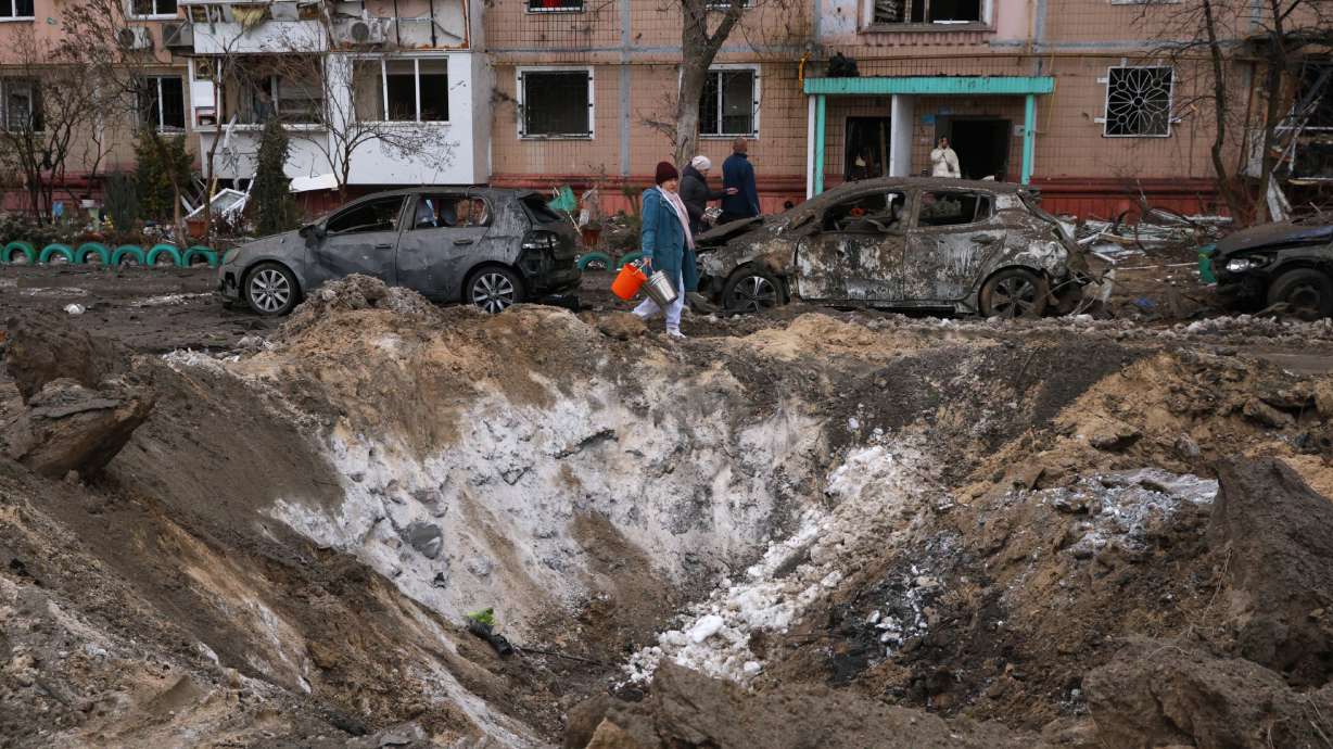 People pass a crater and damaged cars near an apartment building after a Russian attack in Zaporizhzhia, Ukraine, Wednesday.