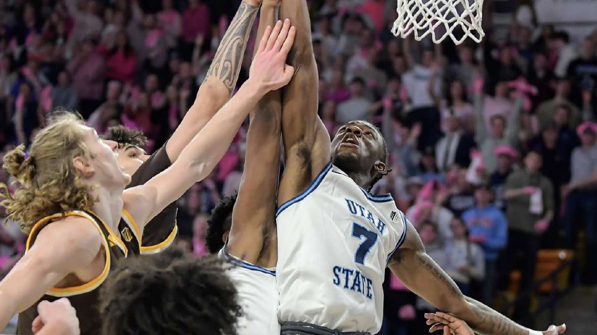 Utah State guard Kolby King (7) tips the ball in for a basket as Wyoming forward Gavin Gores, left, and forward Kiani Saxon defend Wednesday night in the Dee Glen Smith Spectrum.