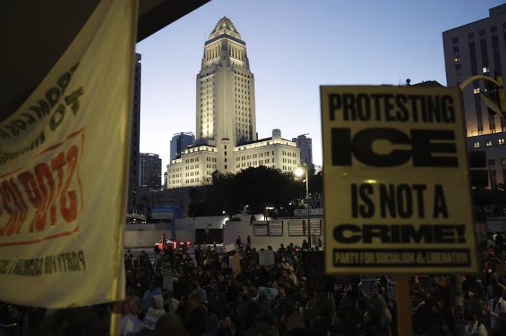 Los Angeles City Hall is seen as demonstrators hold signs during a protest in response to the fatal shooting of 37-year-old Alex Pretti in Minneapolis earlier in the day, Saturday, in Los Angeles.