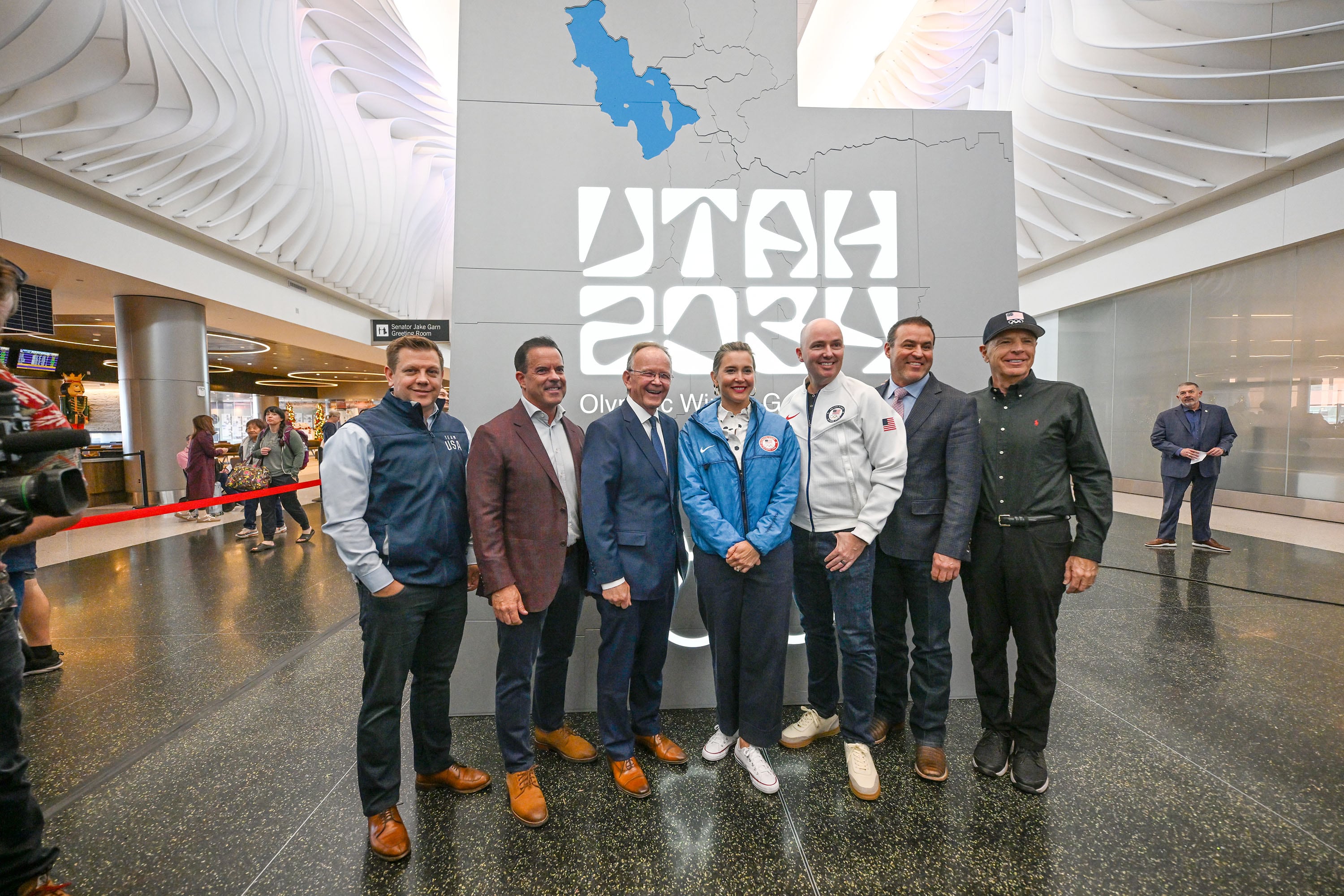 Members of the Organizing Committee for the 2034 Olympic and Paralympic Winter Games, including Steve Starks, Brad Wilson, Stuart Adams, Erin Mendenhall, Gov. Spencer Cox, Mike Schultz, and Fraser Bullock, in front of a new sign inside the Canyon section of the airport as they celebrate 3,000 days until the 2034 Winter Olympics during a ceremony at the Salt Lake City International Airport on Nov. 24, 2025.