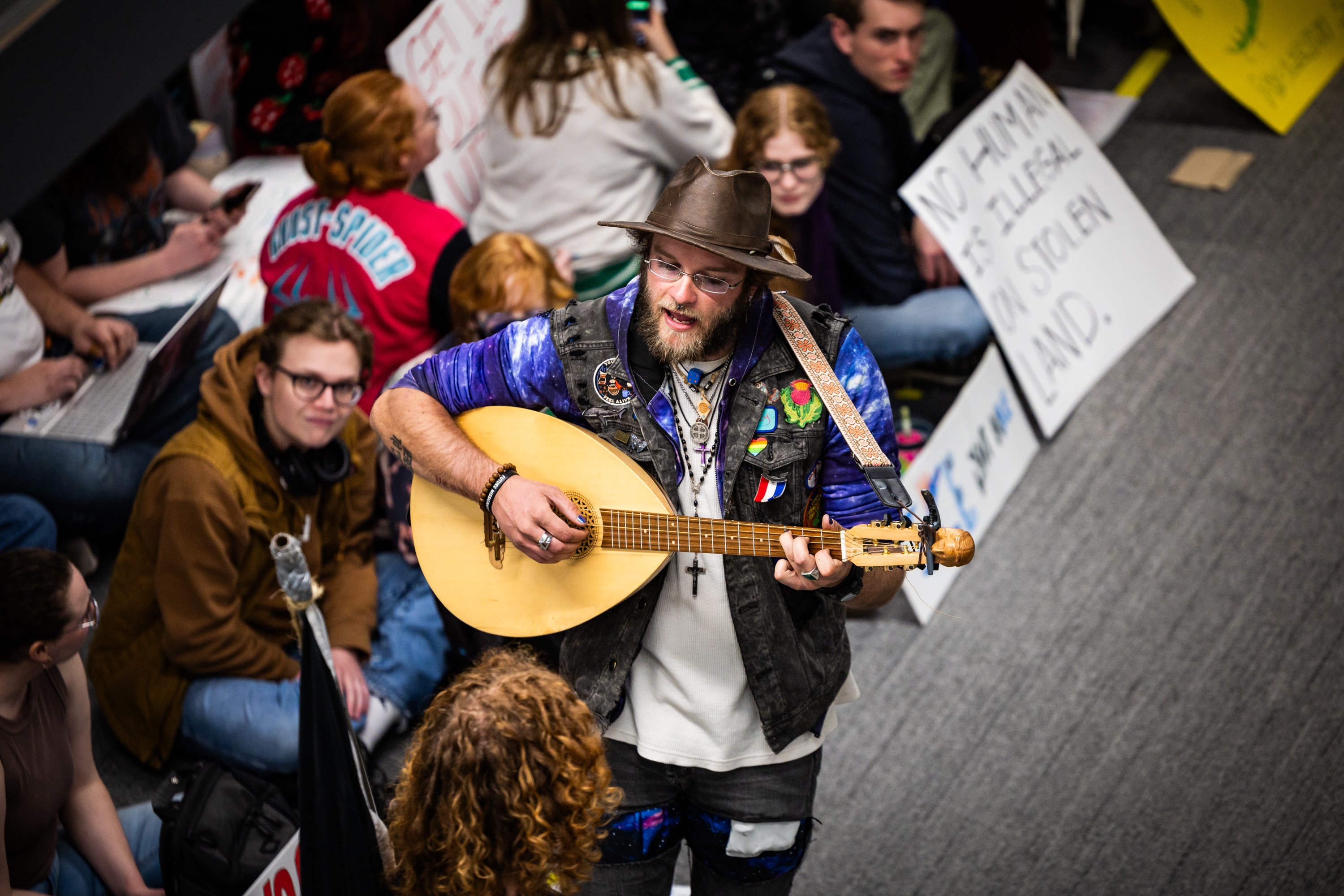 UVU Civil Disobedience Club co-presidents and organizers of the sit-in Harper McGee, bottom left, and Jack McNiven, center, play guitar and sing during a sit-in against Department of Homeland Security recruitment at a job fair across from the Sorensen Center Grand Ballroom in Orem on Wednesday.