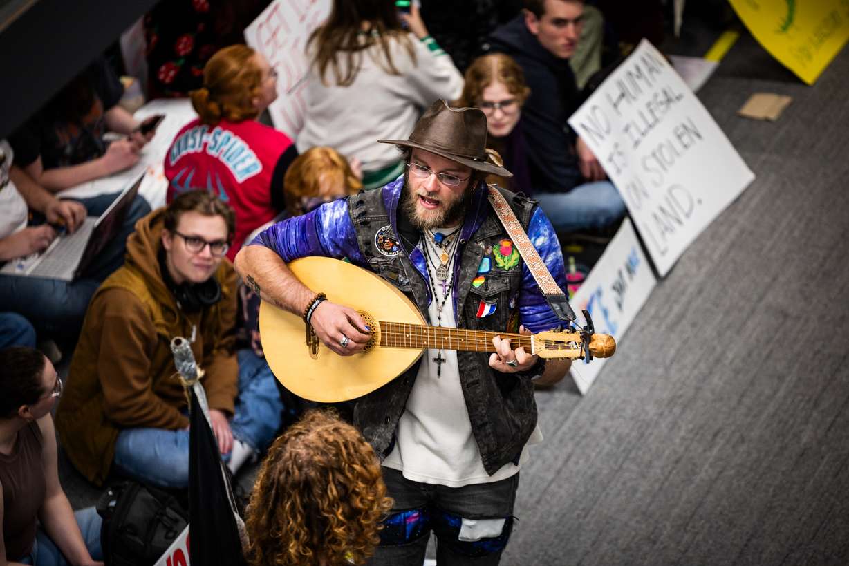UVU Civil Disobedience Club co-presidents and organizers of the sit-in Harper McGee, bottom left, and Jack McNiven, center, play guitar and sing during a sit-in against Department of Homeland Security recruitment at a job fair across from the Sorensen Center Grand Ballroom in Orem on Wednesday.