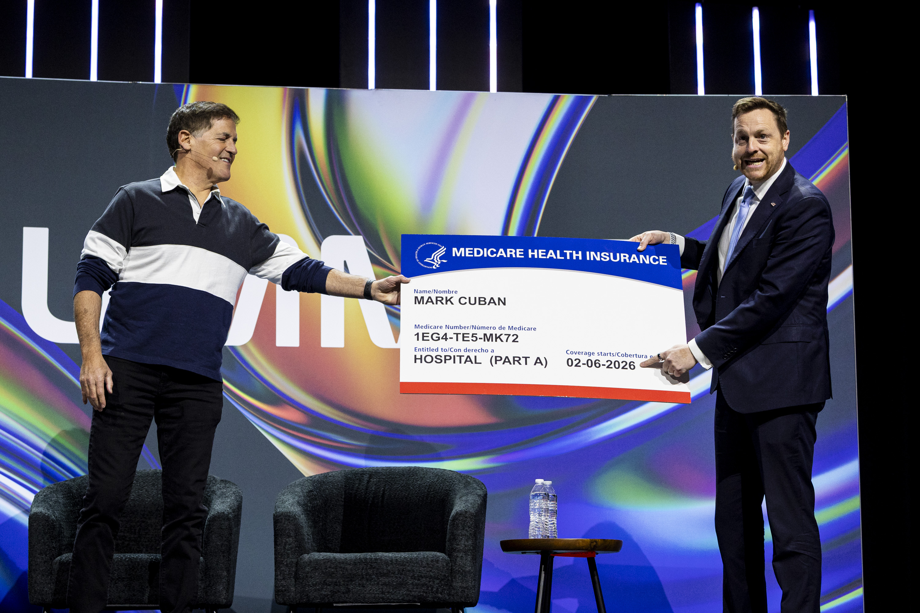 Chris Klomp, director of the Center for Medicare within the U.S. Department of Health and Human Services, right, jokingly gives an oversized Medicare health insurance card to Mark Cuban, co-founder of Cost Plus Drugs and businessman, during the Silicon Slopes Summit in Salt Lake City on Friday.