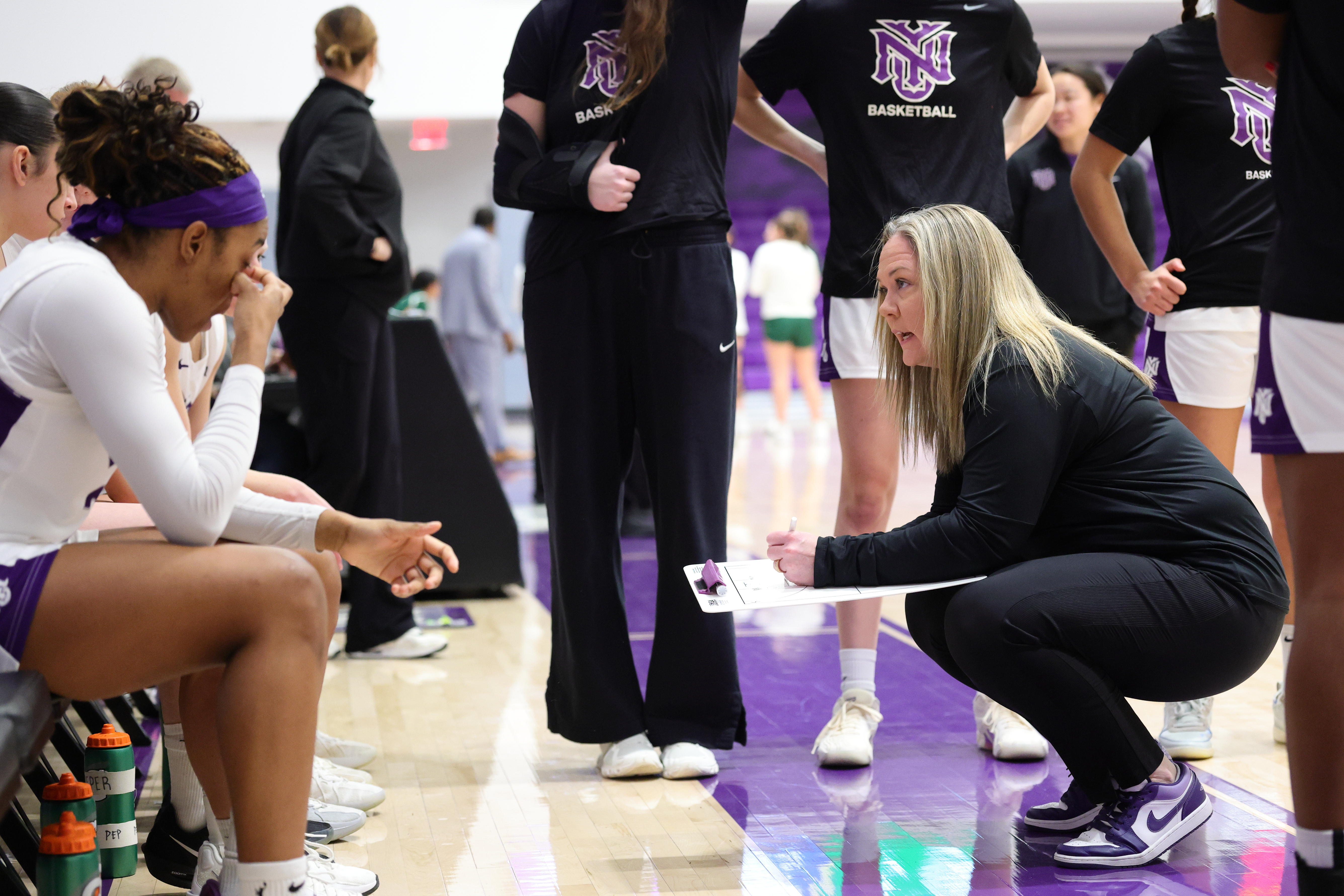 In this image provided by NYU Athletic Communications, NYU coach Meg Barber, right, talks to her players during an NCAA Div III college basketball game against Carnegie Mellon, Sunday, Feb. 1, 2026, in New York. 