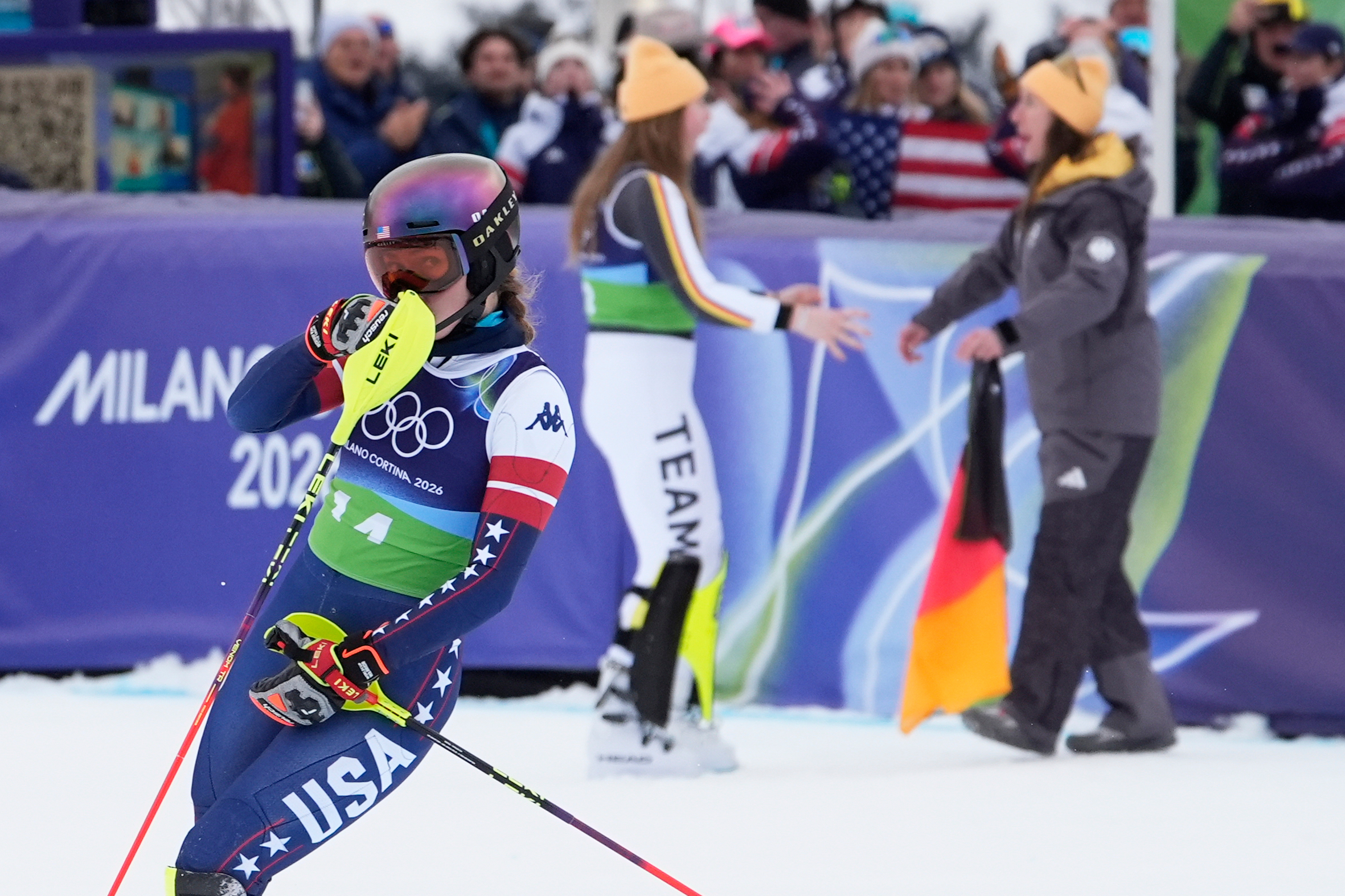 United State's Mikaela Shiffrin reacts as she looks back to see her disappointing time as Germany's Emma Aicher, background left, and Kira Weidle Winkelmann celebrate winning the silver medal in an alpine ski, women's team combined race, at the 2026 Winter Olympics, in Cortina d'Ampezzo, Italy, Tuesday, Feb. 10, 2026. 