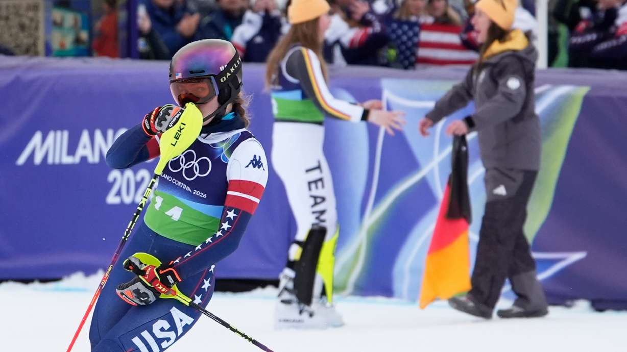 United State's Mikaela Shiffrin reacts as she looks back to see her disappointing time as Germany's Emma Aicher, background left, and Kira Weidle Winkelmann celebrate winning the silver medal in an alpine ski, women's team combined race, at the 2026 Winter Olympics, in Cortina d'Ampezzo, Italy, Tuesday, Feb. 10, 2026.