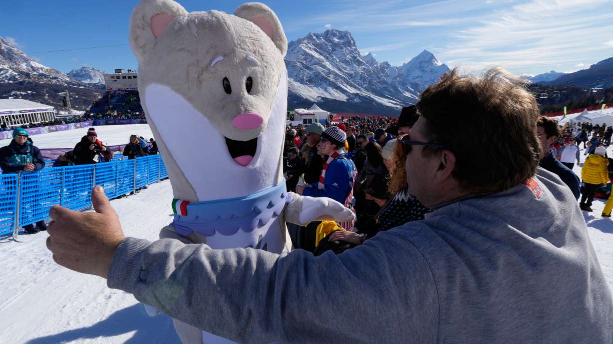 A spectator moves in to hug Olympic mascot Tina prior to an alpine ski women's downhill race, at the 2026 Winter Olympics, in Cortina d'Ampezzo, Italy, Sunday, Feb. 8, 2026..