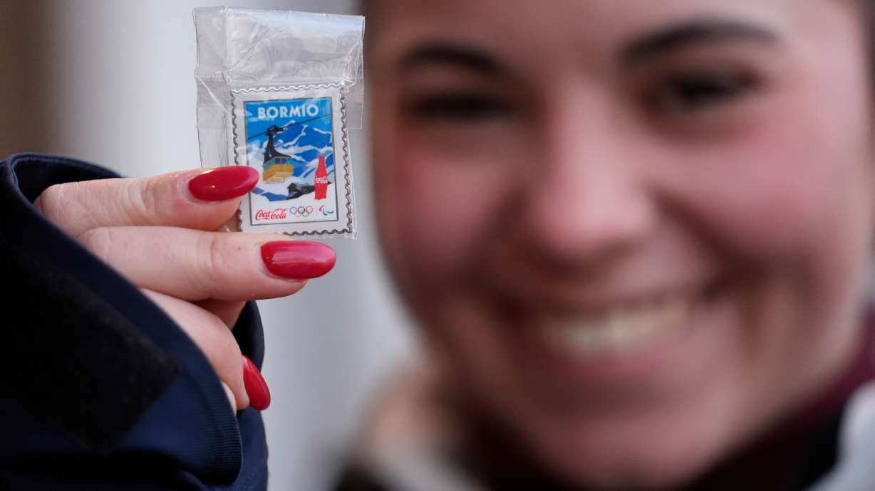 A woman shows a pin she is looking to trade at the 2026 Winter Olympics, in Cortina d'Ampezzo, Italy, Wednesday, Feb. 11, 2026.
