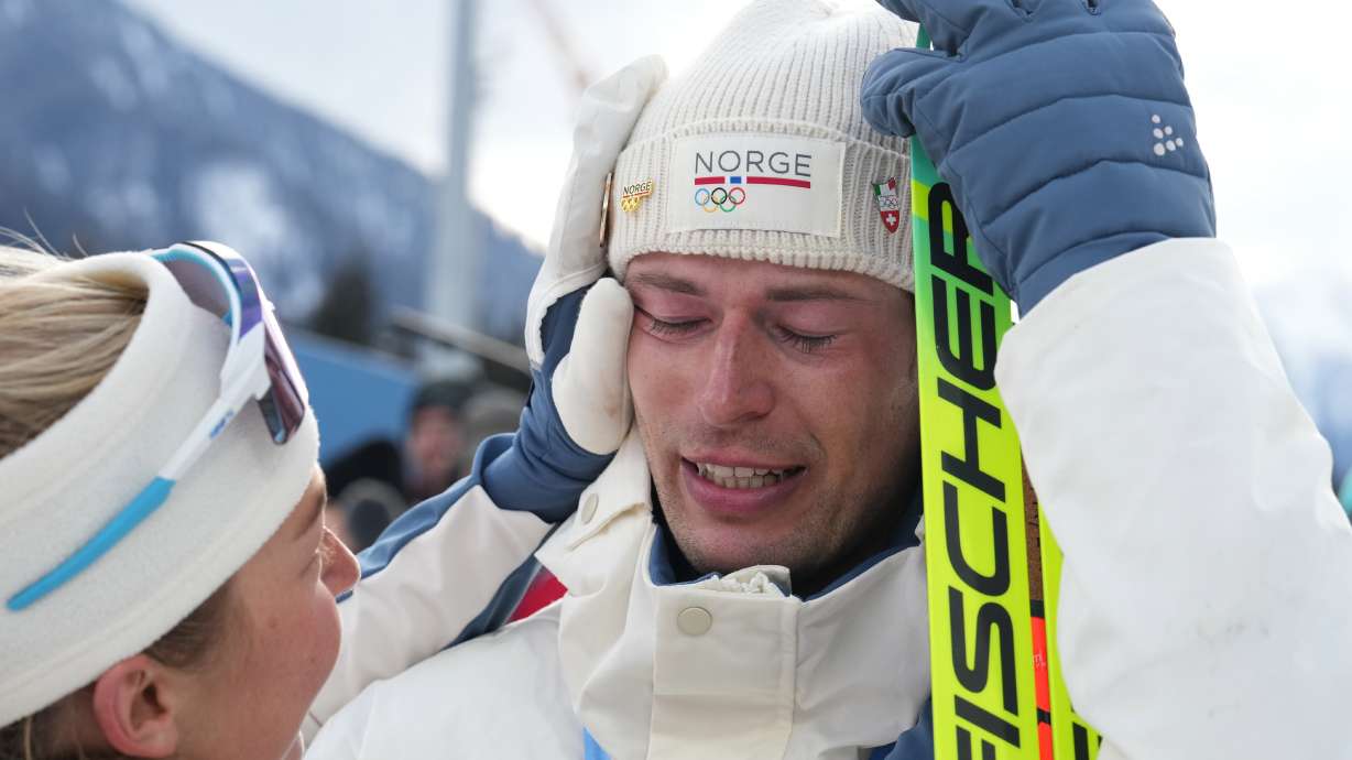 ADDS NAME OF TEAMMATE - Sturla Holm Laegreid, of Norway, reacts after he won bronze as teammate Ingrid Landmark Tandrevold comforts him after the men's 20-kilometer individual biathlon race at the 2026 Winter Olympics in Anterselva, Italy, Tuesday, Feb. 10, 2026.