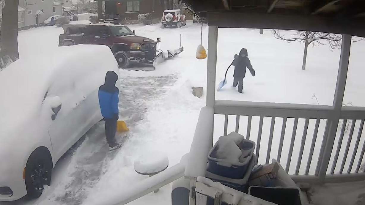 A truck with a snow plow helps a pair of kids finish shoveling their driveway.