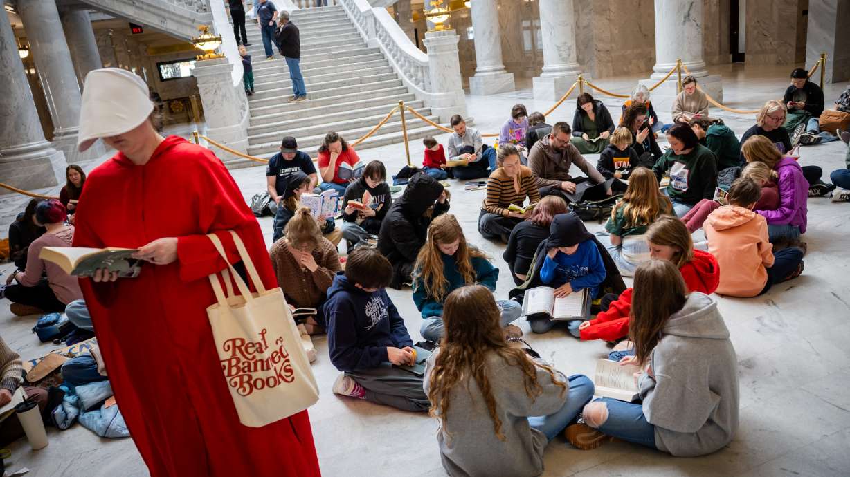 Haley Giddings, dressed in a "The Handmaid's Tale" costume, left, reads at the annual Let Utah Read Read-In, an event advocating for reading and the resistance to book bans, at the Capitol Rotunda in Salt Lake City on Friday.