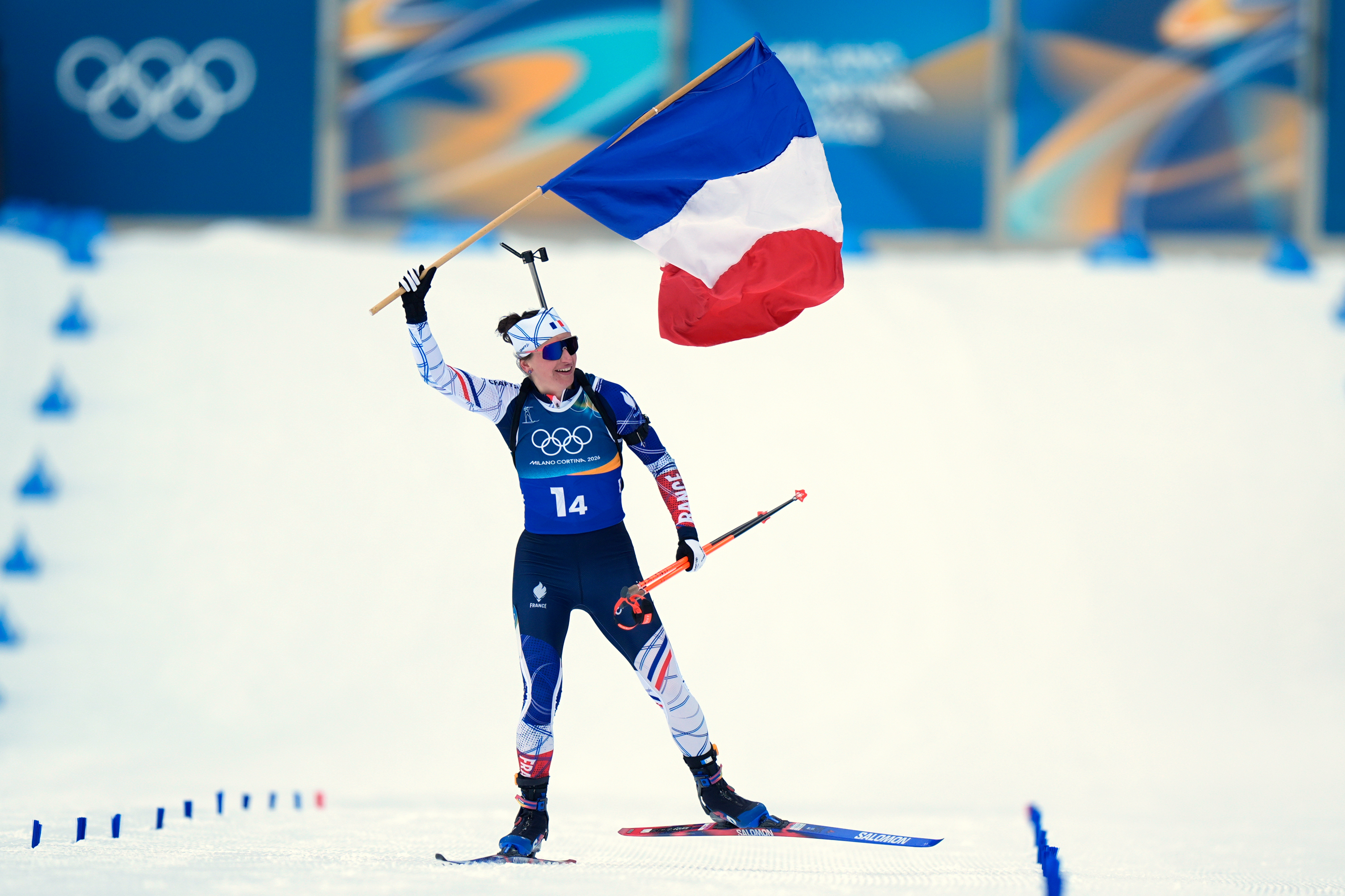 Julia Simon, of France, skis to the finish line with her country's flag for gold in the women's 4x6-kilometer relay biathlon race at the 2026 Winter Olympics in Anterselva, Italy, Wednesday, Feb. 18, 2026. 