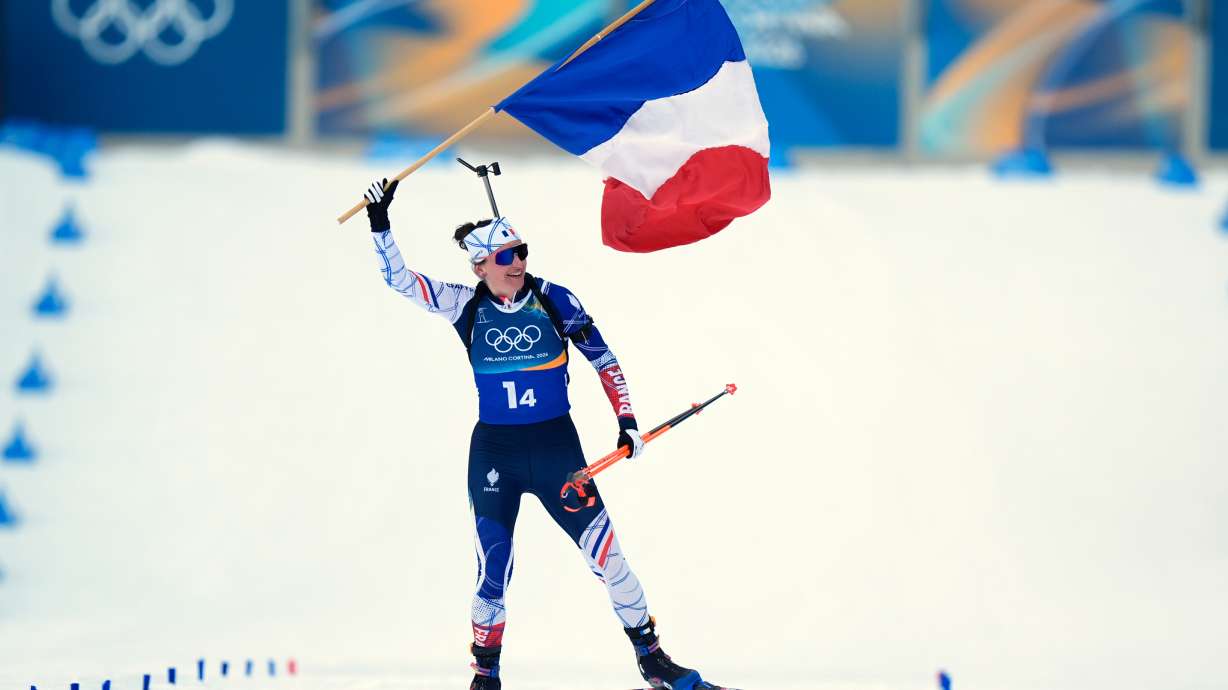 Julia Simon, of France, skis to the finish line with her country's flag for gold in the women's 4x6-kilometer relay biathlon race at the 2026 Winter Olympics in Anterselva, Italy, Wednesday, Feb. 18, 2026.