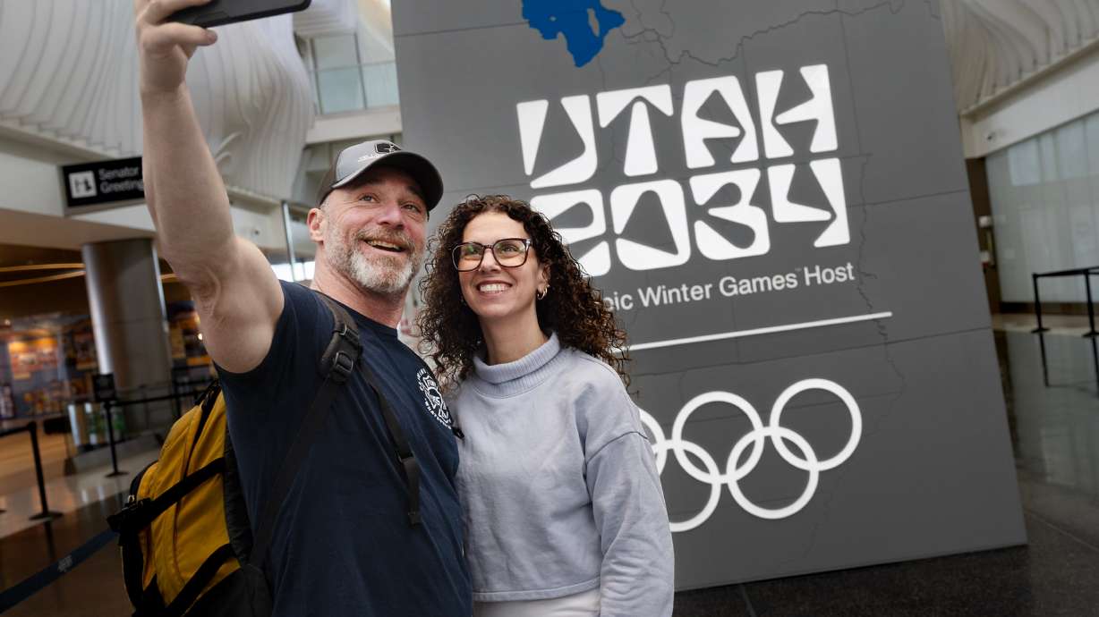 Craig and Annemarie Mosia of Long Island, N.Y., take a photo in front of the “Utah 2034” Olympics logo at the Salt Lake City International Airport on Friday.