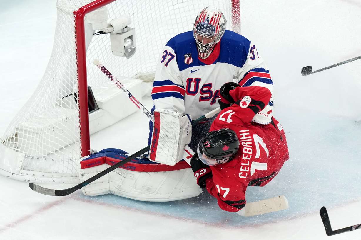 Canada's Macklin Celebrini (17) slides into United States goalkeeper Connor Hellebuyck (37) during the third period of the men's ice hockey gold medal game at the 2026 Winter Olympics in Milan, Italy, Sunday.