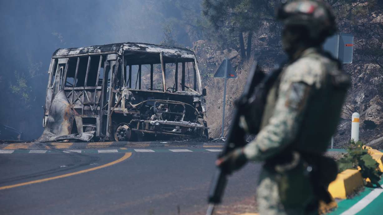 A soldier stands guard by a charred vehicle after it was set on fire, in Cointzio, Michoacán state, Mexico, Sunday, following the death of the leader of the Jalisco New Generation Cartel, Nemesio Oseguera, known as "El Mencho."