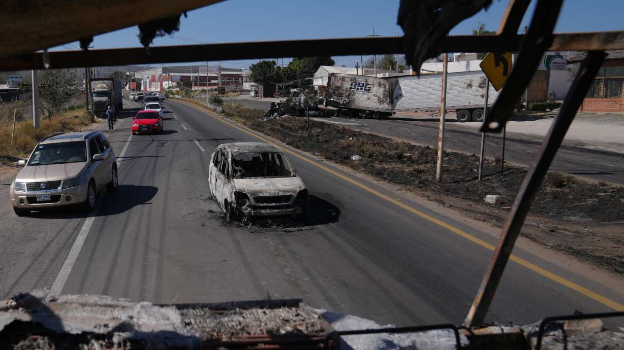 Vehicles pass a burned car a day after the Mexican army killed the leader of the Jalisco New Generation Cartel, Nemesio Oseguera Cervantes, known as "El Mencho," in Guadalajara, Mexico, Monday, Feb. 23, 2026.