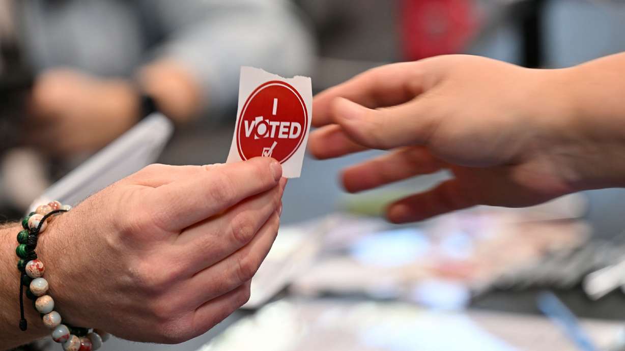 A worker hands an “I Voted” sticker to a voter at the Salt Lake County Library in Kearns on Nov. 4. While President Trump implored Republicans on Tuesday to pass Utah Sen. Mike Lee's SAVE Act, the reality of doing it is complicated.