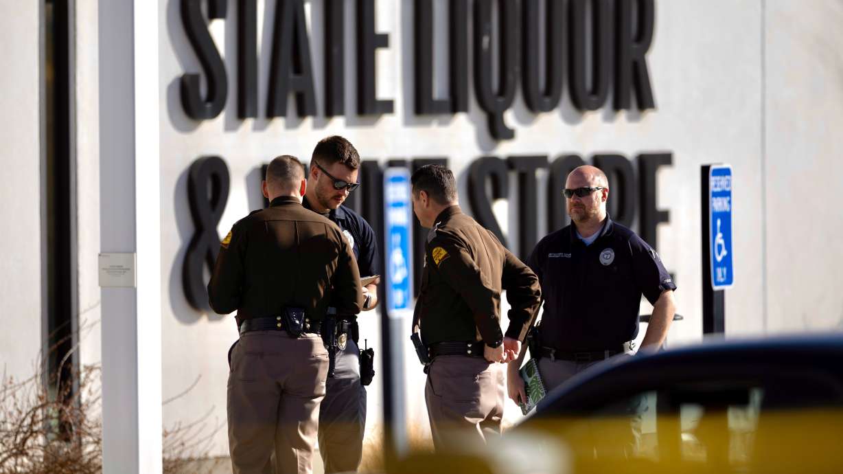 Police officers and others stand outside the scene of a shooting at the state liquor store in Taylorsville on Thursday.