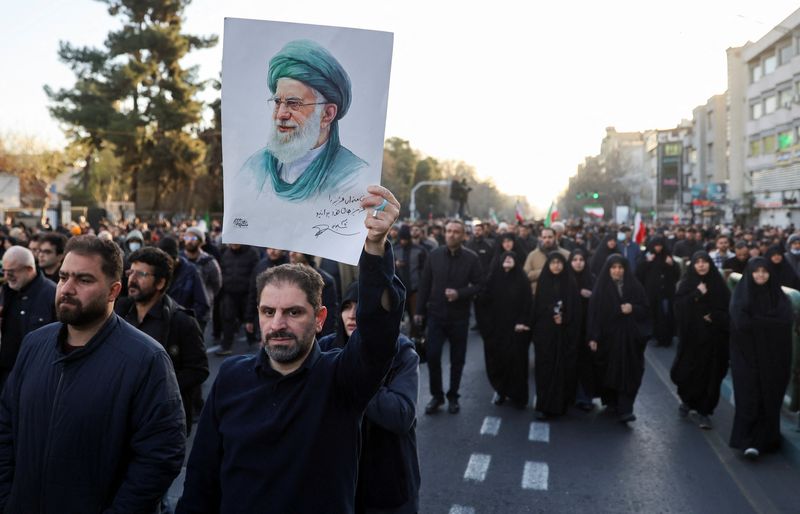 A man holds up a picture of Iran's Supreme Leader Ayatollah Ali Khamenei as people gather after  Khamenei was killed in Israeli and U.S. strikes on Saturday, in Tehran, Iran, Sunday. Israeli strikes continued against Iran on Sunday morning.