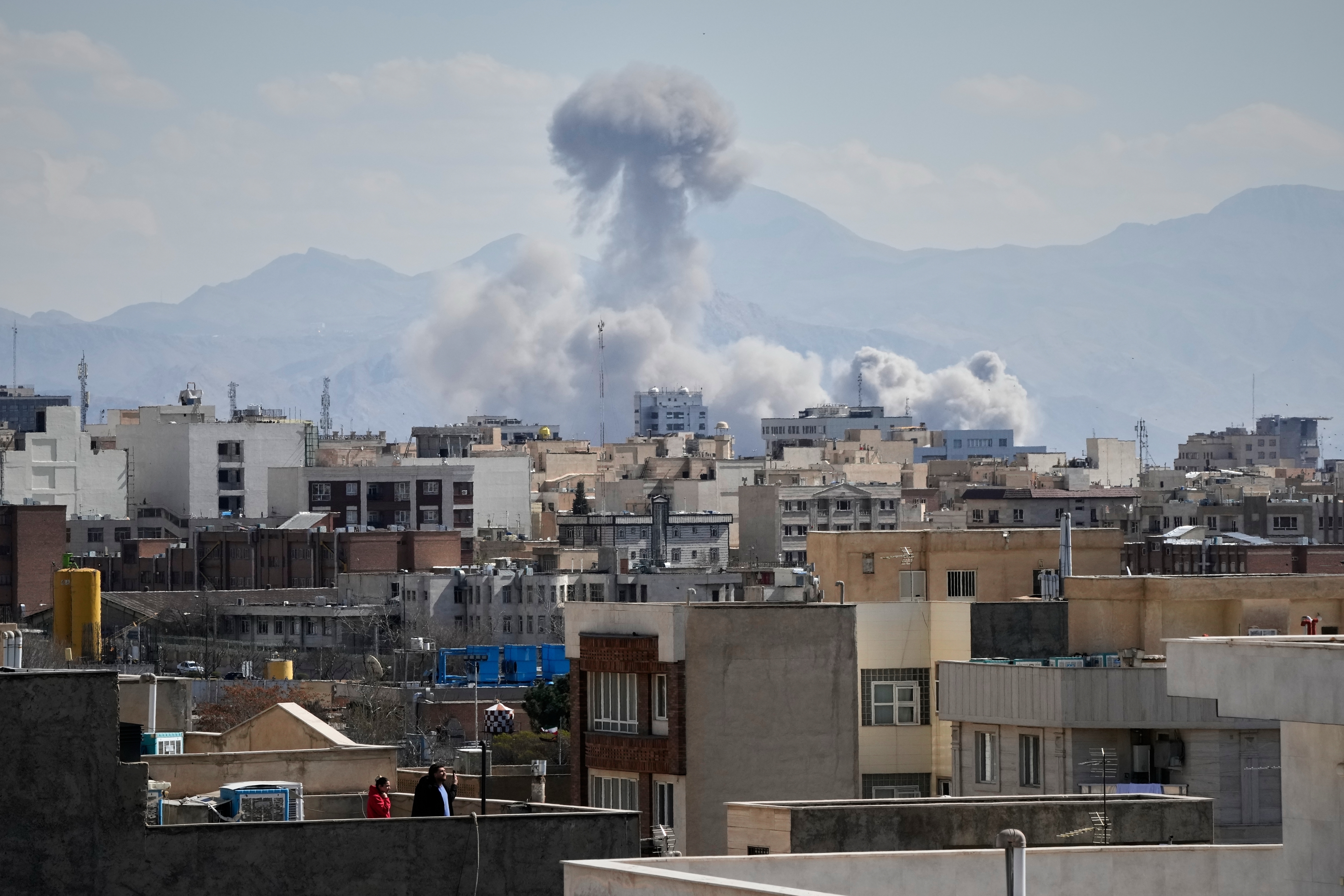 People watch from a rooftop as a plume of smoke rises after a strike in Tehran, Iran, Sunday, March 1, 2026.