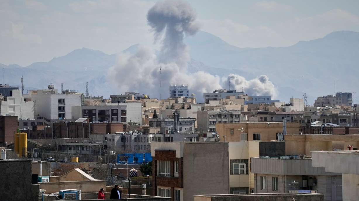 People watch from a rooftop as a plume of smoke rises after a strike in Tehran, Iran, Sunday, March 1, 2026.