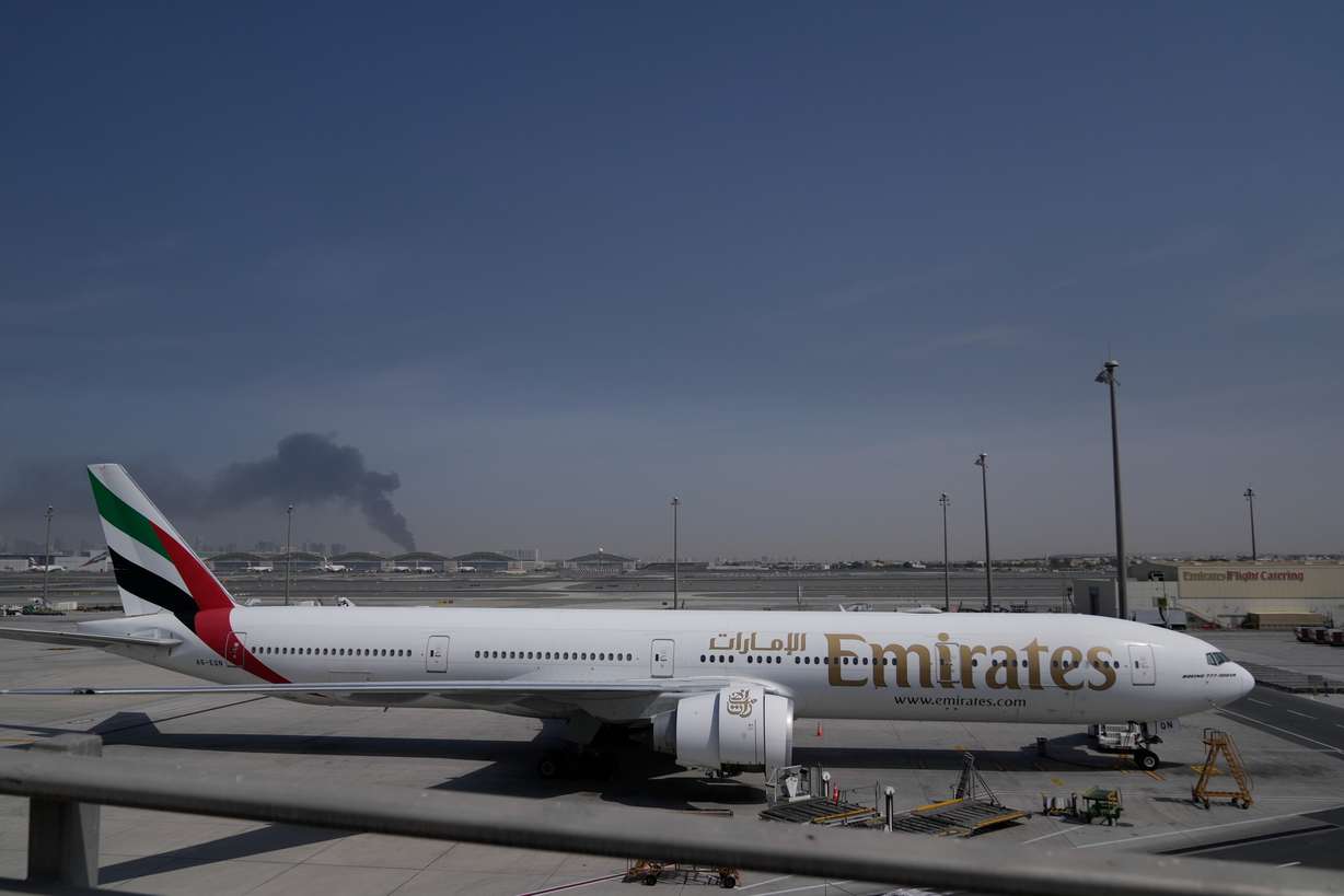 A plume of smoke caused by an Iranian strike is seen in the background an an Emirates plane is parked at the Dubai International Airport after its closure in Dubai, United Arab Emirates, Sunday. Four Utahns are stuck in the Middle East as the Iran war has upended travel.