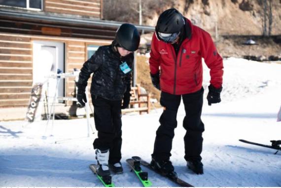 Bob Carlson helps guide Greyson Ward, who is new to skiing, to put on his skis at Kelly Canyon on Friday.