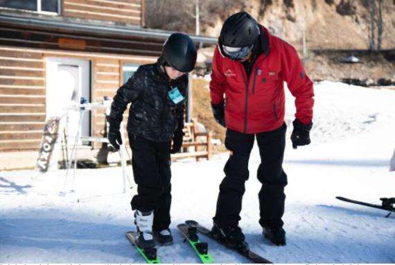 Bob Carlson helps guide Greyson Ward, who is new to skiing, to put on his skis at Kelly Canyon on Friday.