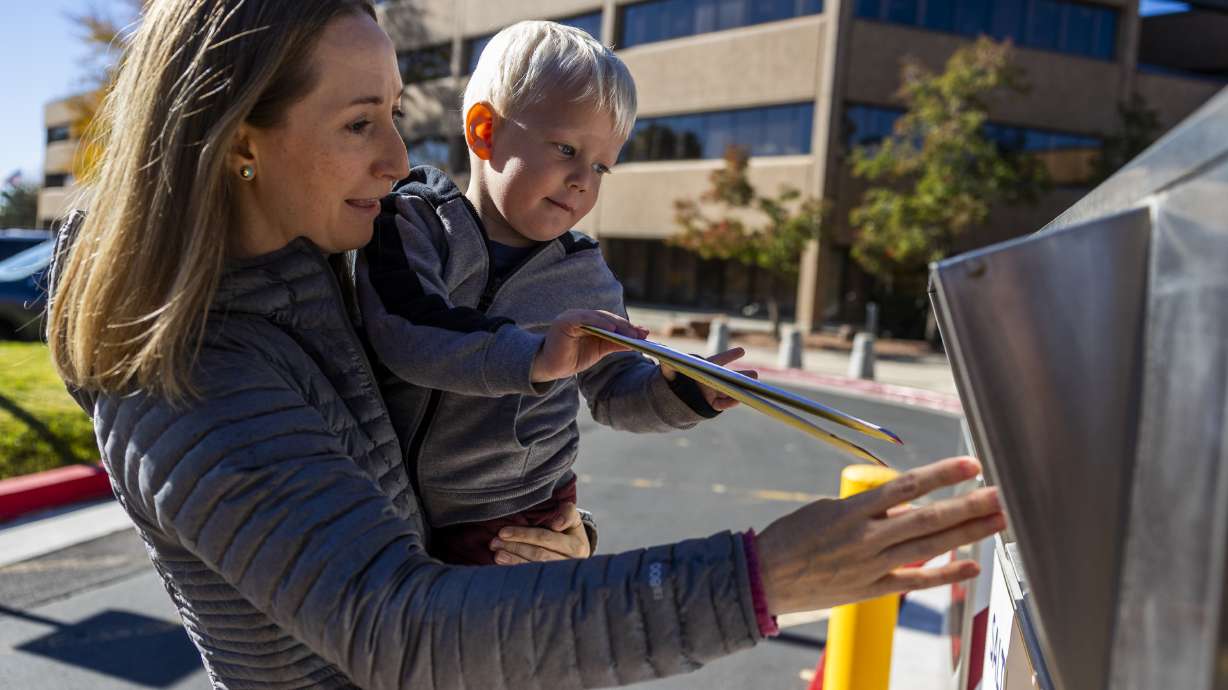 Katherine Kitterman holds her 2-year-old son, Ethan Roberts, as he places her ballot in a drop box in Salt Lake City on Nov. 4, 2024. A Senate committee shot down a bill that would have required Utah voters to turn in mailed ballots by showing their ID.