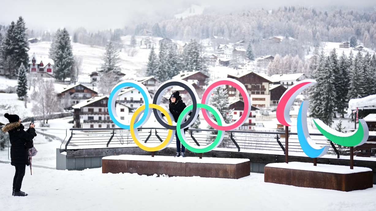 FILE - People take photos in front of the Milan Cortina Winter Olympics and Paralympics rings, in Cortina D'Ampezzo, on Nov. 20, 2025.