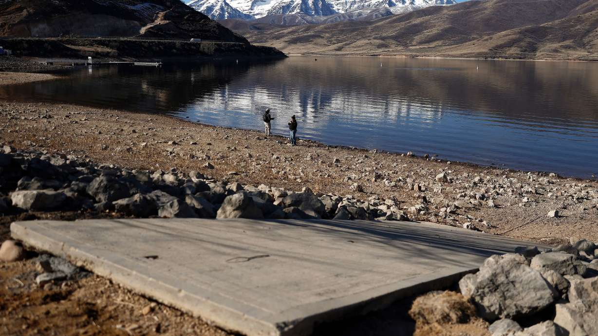 People fish along the Deer Creek Reservoir with the snow-capped Wasatch Mountains in the distance on Feb. 7 near Heber City. Utah, like other states in the West, has experienced a record-setting warm winter and snow drought.