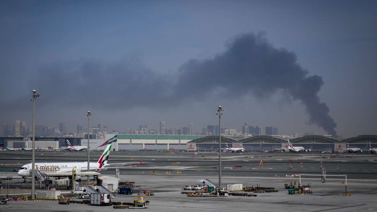 A plume of smoke caused by an Iranian strike is seen in the background as Emirates planes are parked at Dubai International Airport after its closure in Dubai, United Arab Emirates, March 1.