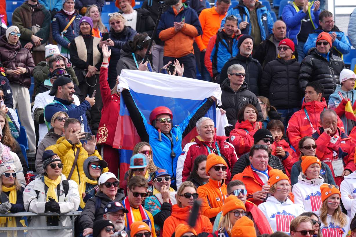 A fan holds up a Russian flag as Varvara Voronchikhina, of Russia, climbs on the podium to receive her gold medal for the alpine skiing women's super-G standing at the 2026 Winter Paralympics, in Cortina d'Ampezzo, Italy, Monday.