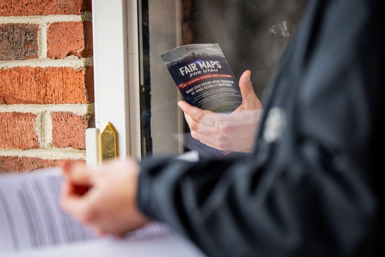 Riley Beesley, vice chairman of the Utah Federation of College Republicans, right, hands Nicasio Perna, center, a flyer after knocking on his door during a Turning Point Action signature gathering event to repeal Proposition 4 at Union Park in Midvale on Feb. 12, 2026. Perna signed the petition.