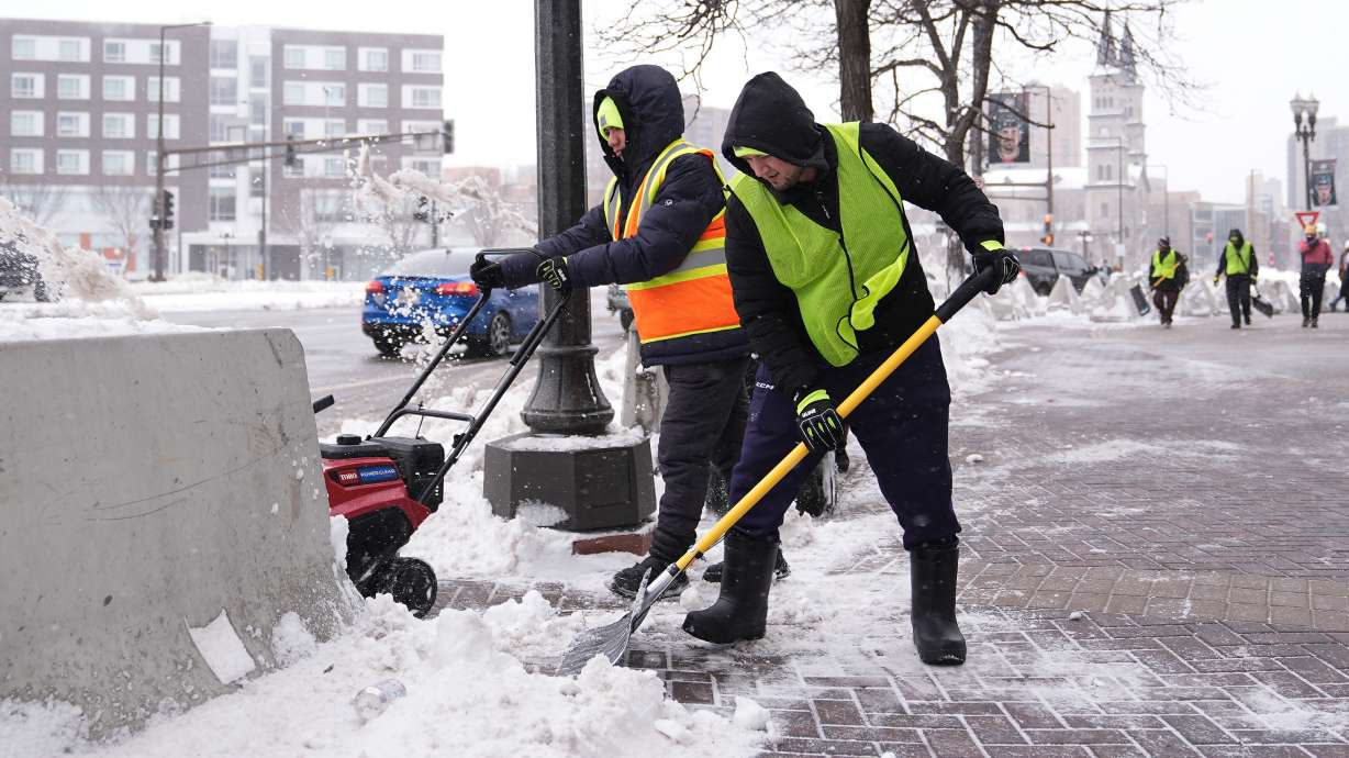 Workers clear snow off the ground on Sunday in St. Paul, Minn.