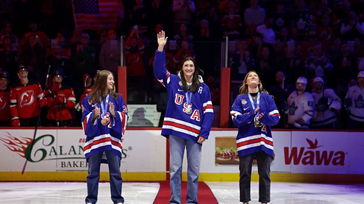United States women's gold medal hockey players Megan Keller, center, Aerin Frankel, left, and Haley Winn, right, acknowledge the crowd before a ceremonial puck drop ahead of an NHL hockey game Wednesday, March 4, 2026, in Newark, N.J.