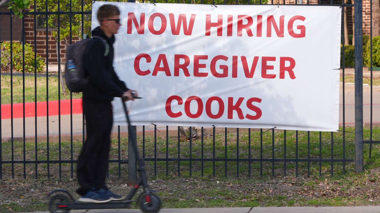 A now hiring sign sits by the sidewalk as a rider on a scooter passes in Garland, Texas, Monday. A new Gallup survey finds that Americans' outlook on the job market is increasingly pessimistic.