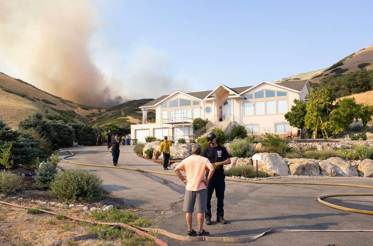 A Salt Lake City firefighter tells a local resident to evacuate while the flames from a wildfire burning around Ensign peak grow closer to his home on Twickenham Drive in Salt Lake City on July 20, 2024. Officials are urging residents to be on high alert and be prepared to evacuate if necessary this fire season.