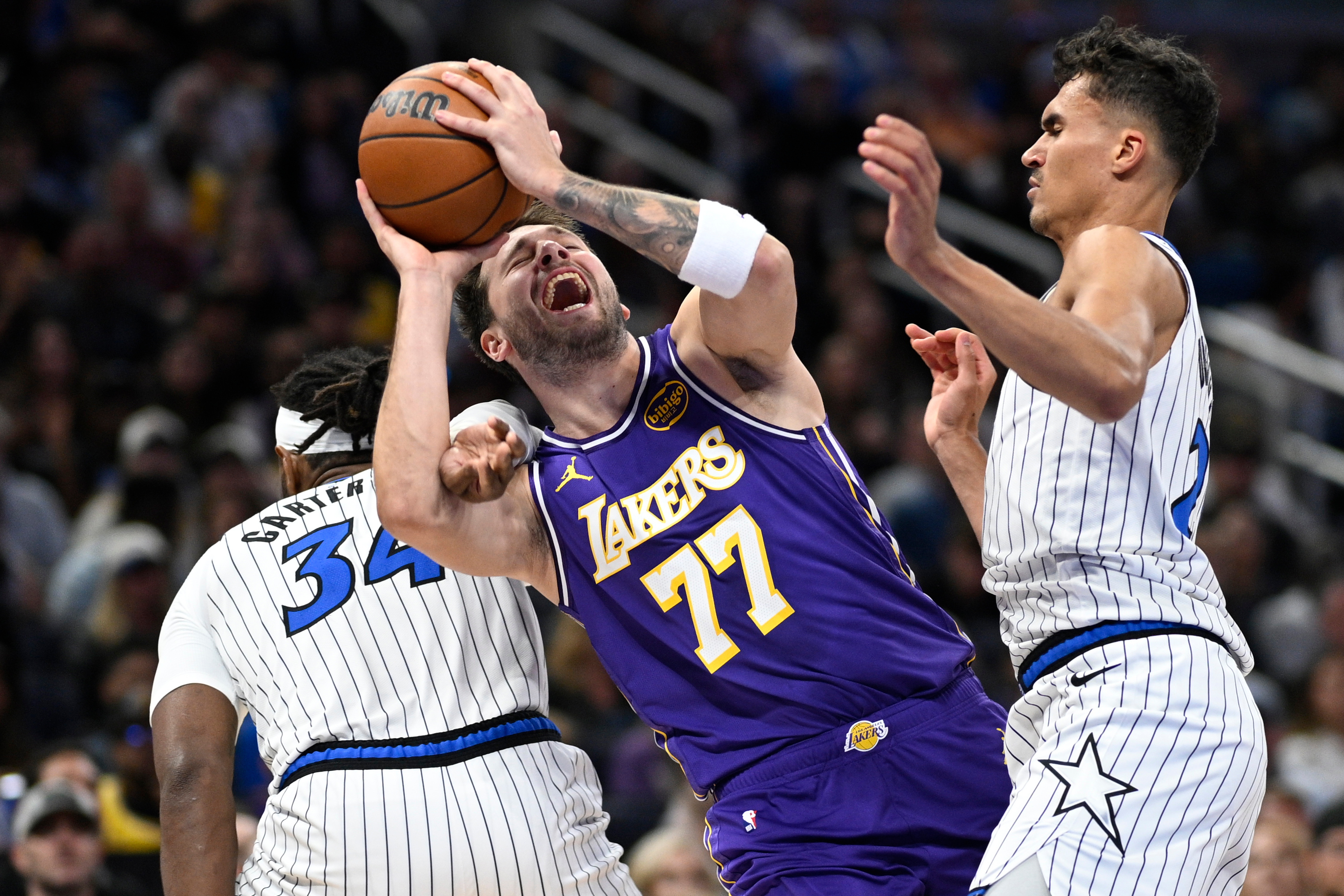 Los Angeles Lakers guard Luka Doncic (77) is fouled by Orlando Magic center Wendell Carter Jr. (34) as Magic forward Tristan da Silva, right, helps defend during the first half of an NBA basketball game, Saturday, March 21, 2026, in Orlando, Fla.