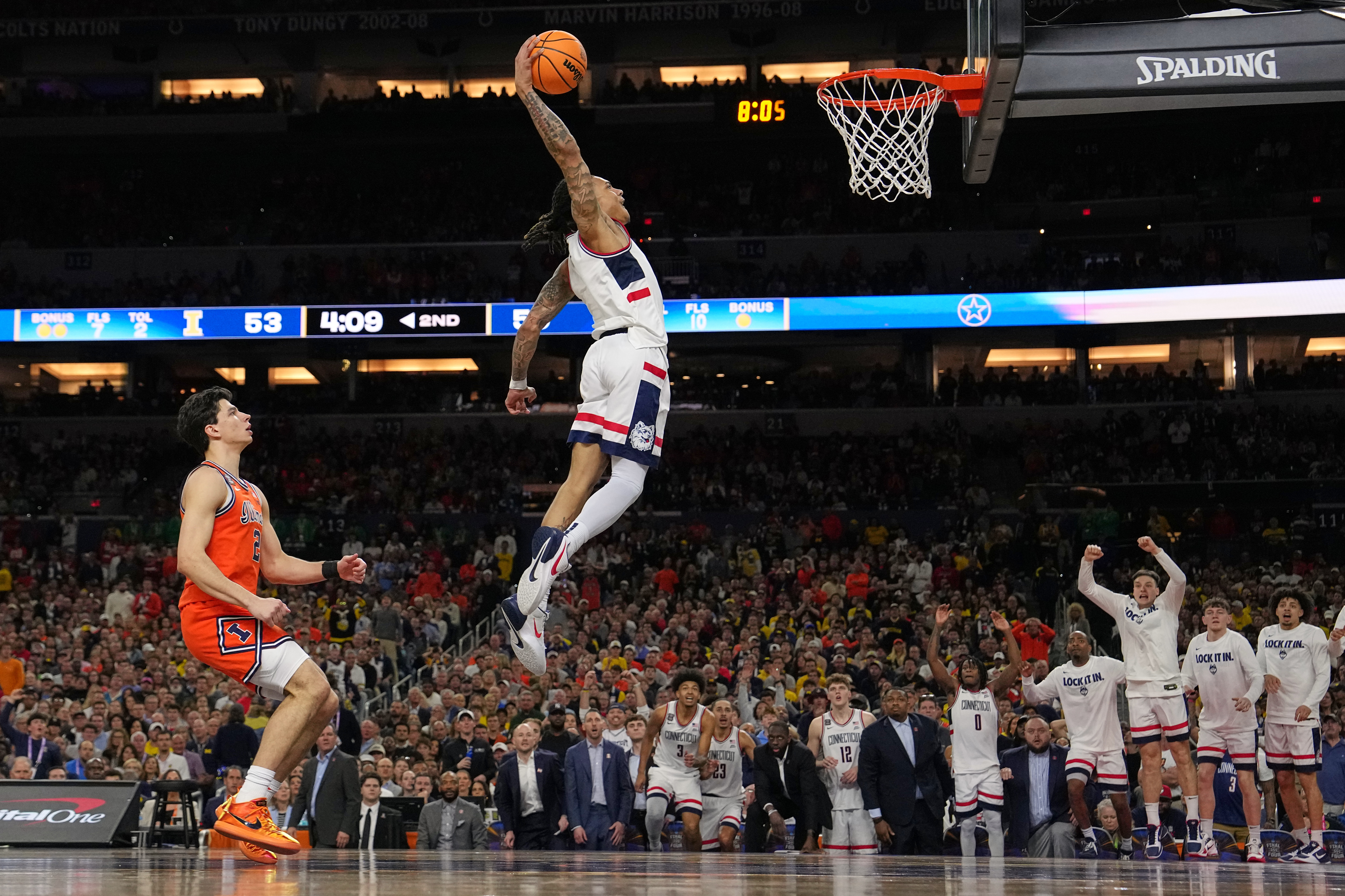 UConn's Solo Ball (1) dunks as Illinois' Andrej Stojakovic, left, watches during the second half of an NCAA college basketball tournament semifinal game at the Final Four, Saturday, April 4, 2026, in Indianapolis.