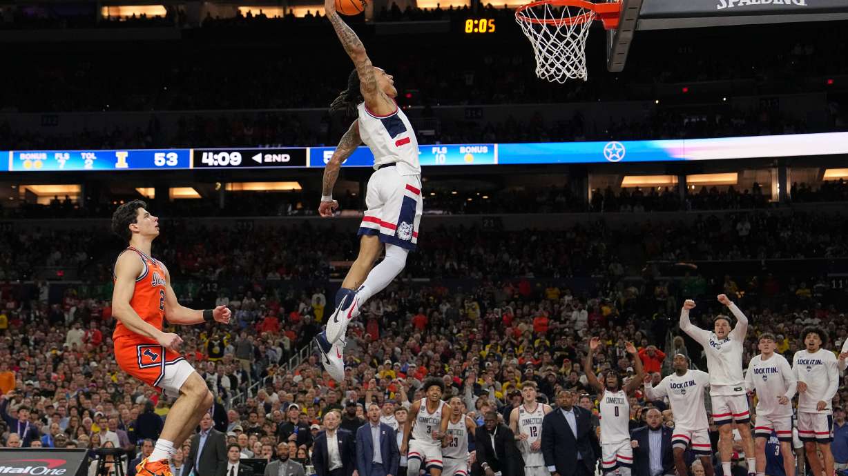 UConn's Solo Ball (1) dunks as Illinois' Andrej Stojakovic, left, watches during the second half of an NCAA college basketball tournament semifinal game at the Final Four, Saturday, April 4, 2026, in Indianapolis.