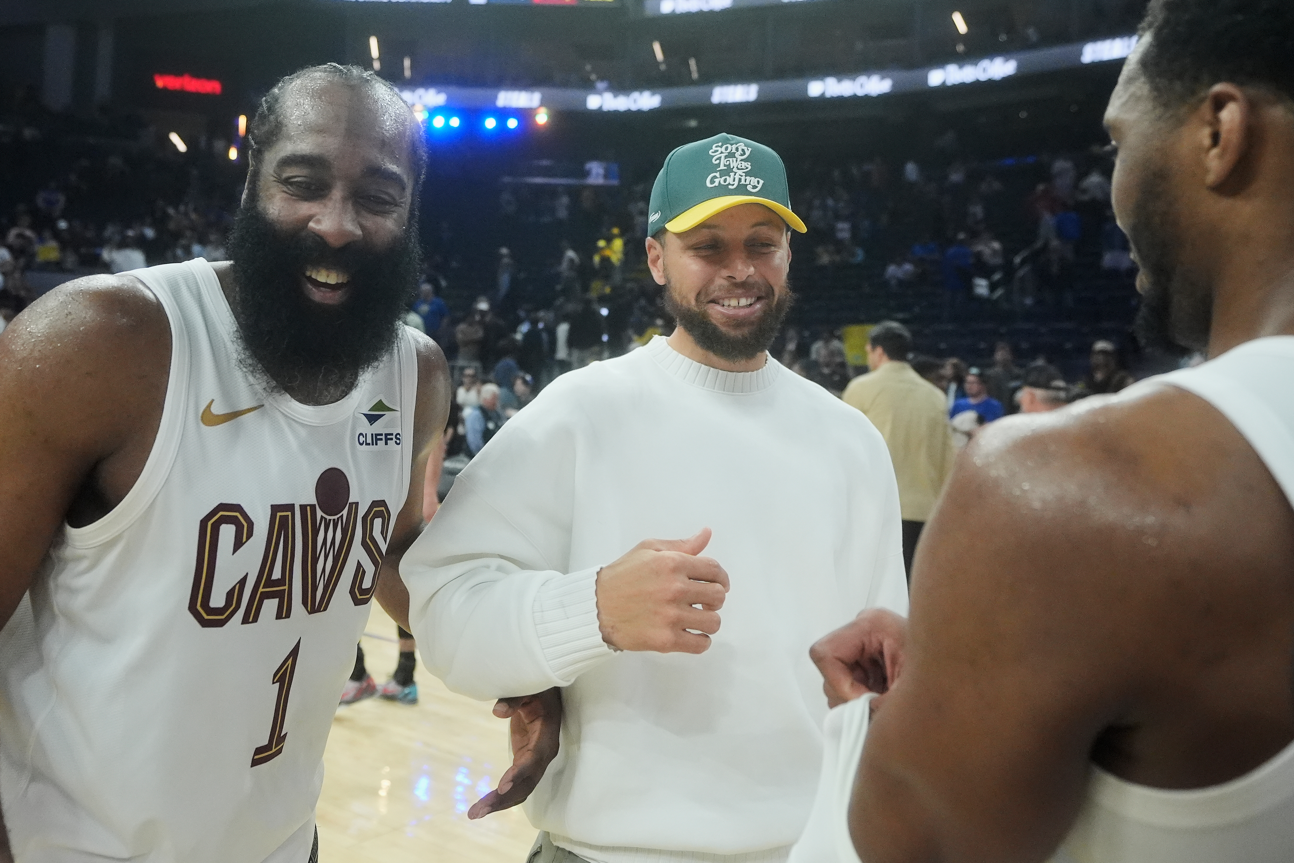Injured Golden State Warriors guard Stephen Curry, middle, smiles while talking with Cleveland Cavaliers guard James Harden (1) and guard Donovan Mitchell after an NBA basketball game in San Francisco, Thursday, April 2, 2026.