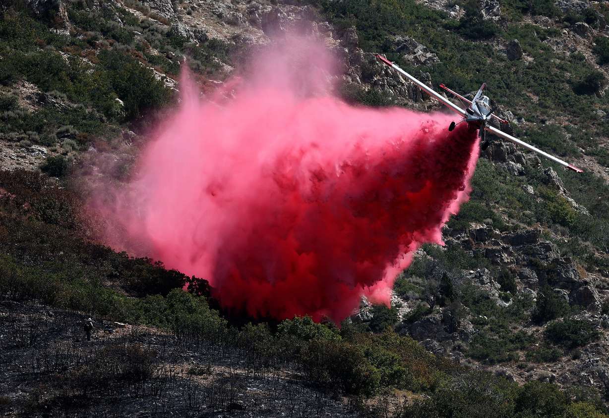 A firefighter watches as a plane drops fire retardant on the Willard Peak wildfire in the mountains above North Ogden on Aug. 14, 2025.
