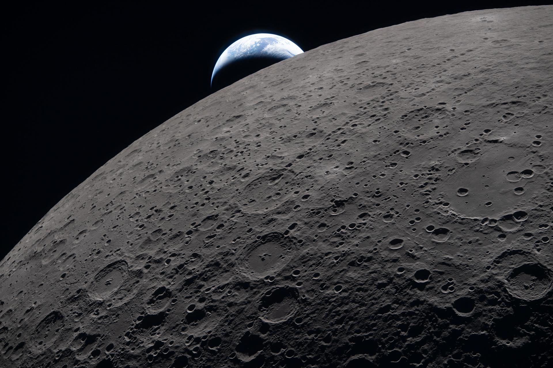 The lunar surface fills the frame in sharp detail, as seen during the Artemis II lunar flyby, while a distant Earth sets in the background.