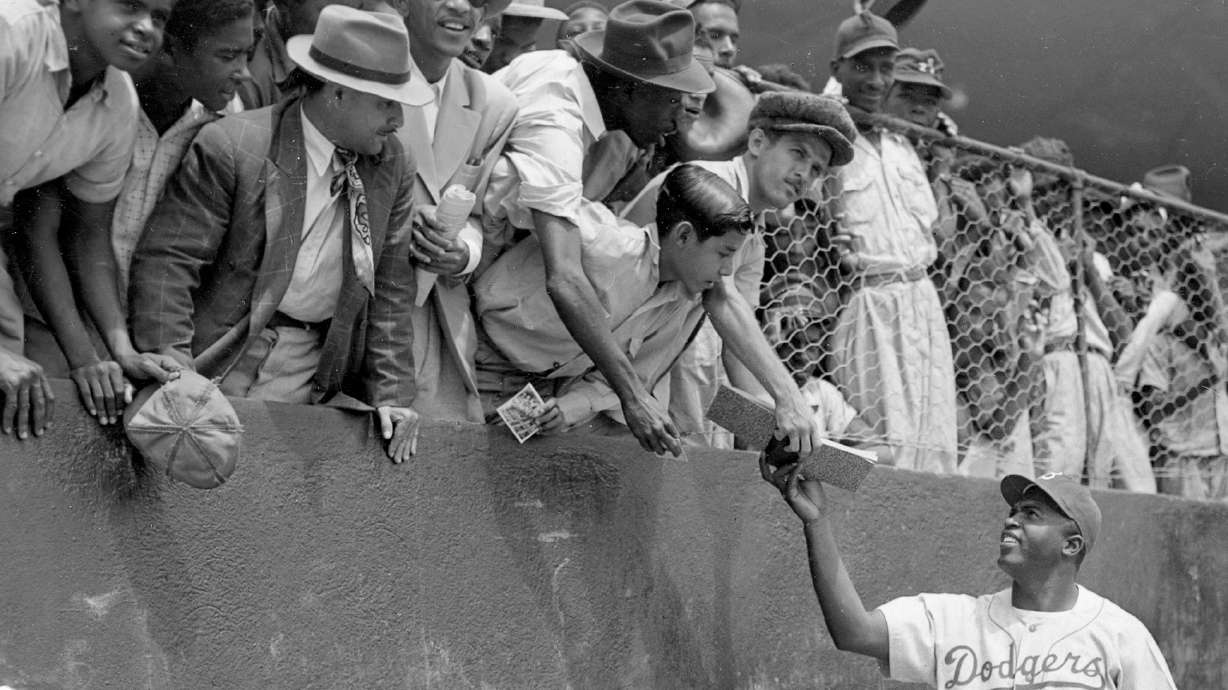 FILE - Jackie Robinson, first baseman of the Brooklyn Dodgers, returns an autograph book to a fan in the stands, during the Dodgers' spring training in Ciudad Trujillo, now Santo Domingo, in the Dominican Republic, on March 6, 1948.
