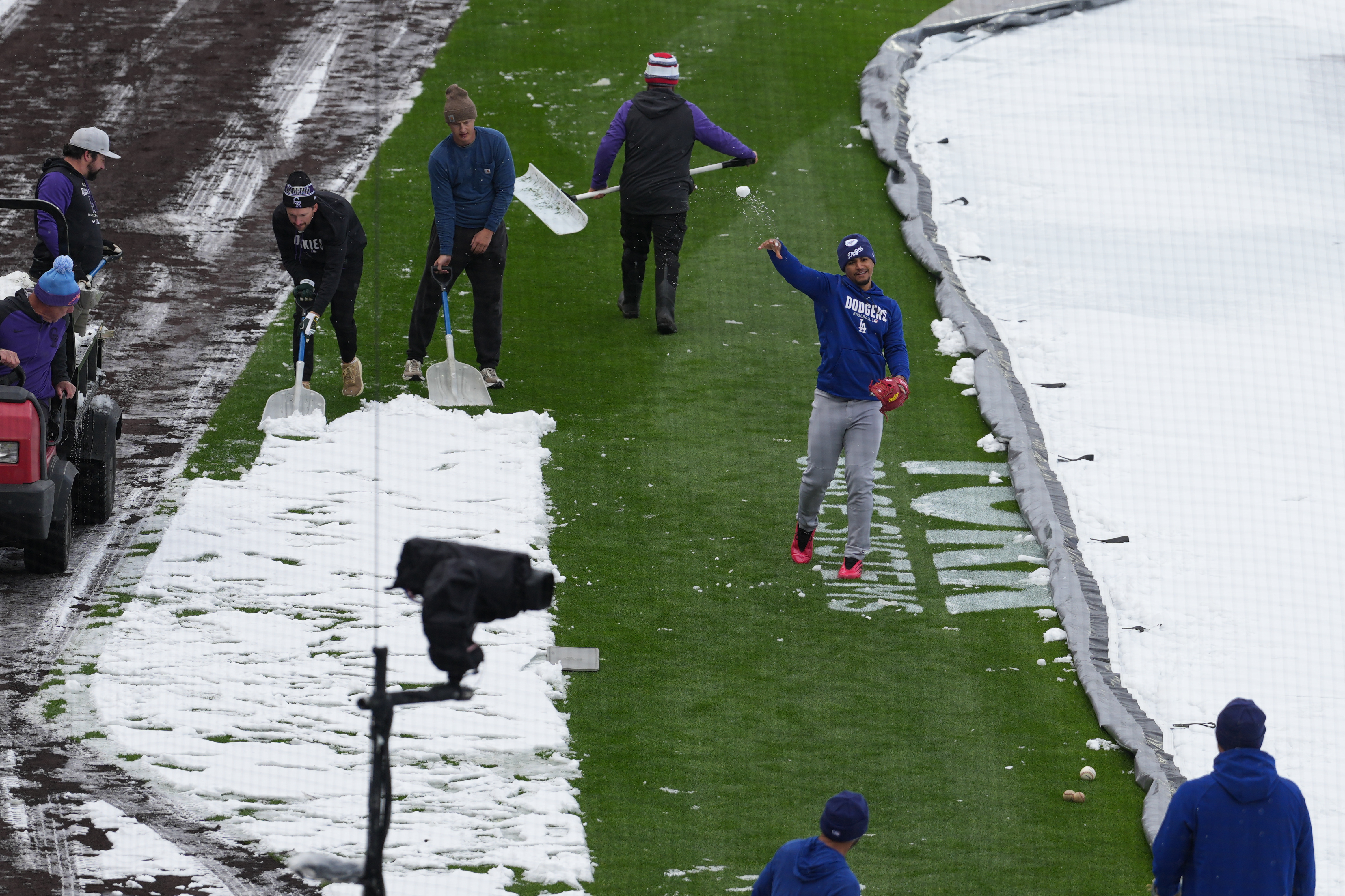 As the grounds crew works around him, Los Angeles Dodgers third baseman Santiago Espinal tosses a snowball at a coach while warming up to face the Colorado Rockies in a baseball game after a spring storm blanketed the intermountain West with a light covering of snow Friday, April 17, 2026, in Denver. 