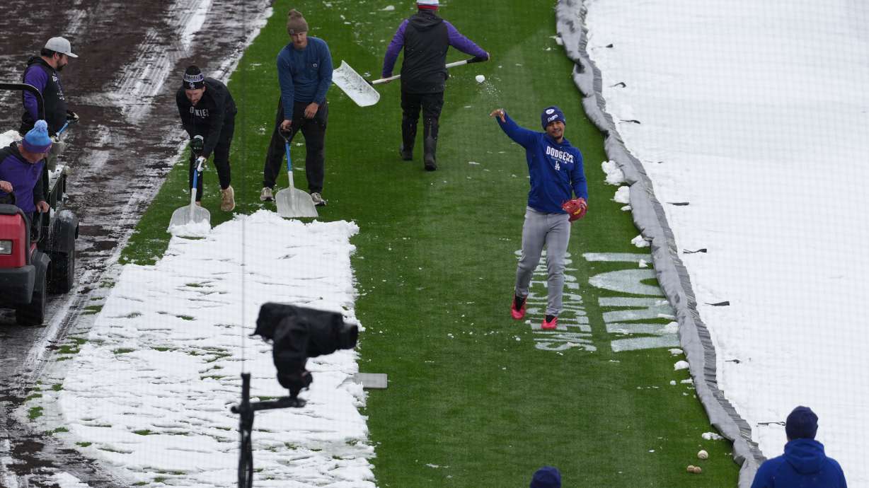 As the grounds crew works around him, Los Angeles Dodgers third baseman Santiago Espinal tosses a snowball at a coach while warming up to face the Colorado Rockies in a baseball game after a spring storm blanketed the intermountain West with a light covering of snow Friday, April 17, 2026, in Denver.
