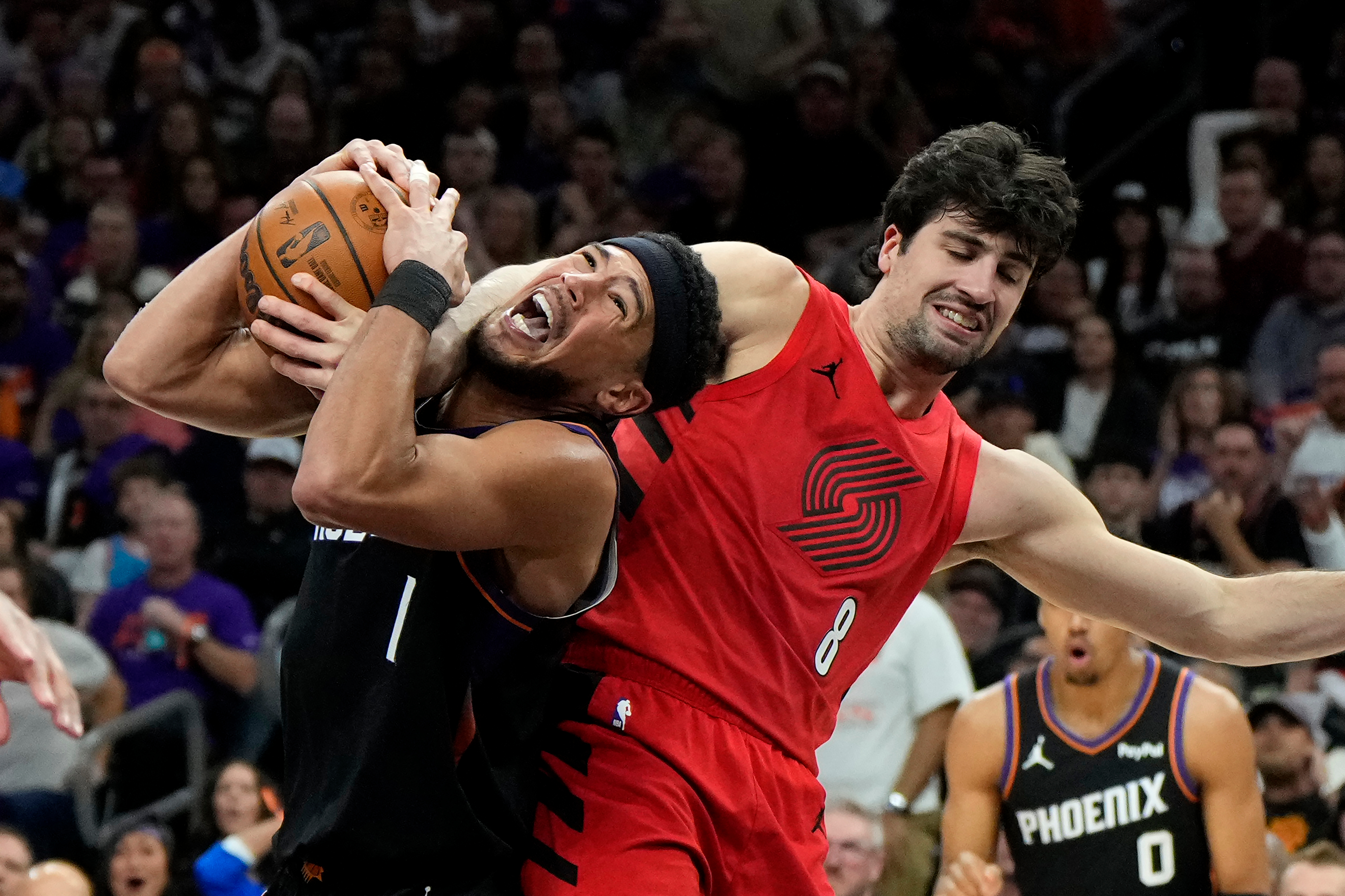 Phoenix Suns guard Devin Booker (1) gets fouled by Portland Trail Blazers forward Deni Avdija (8) during the second half of an NBA play-in tournament basketball game, Tuesday, April 14, 2026, in Phoenix. 